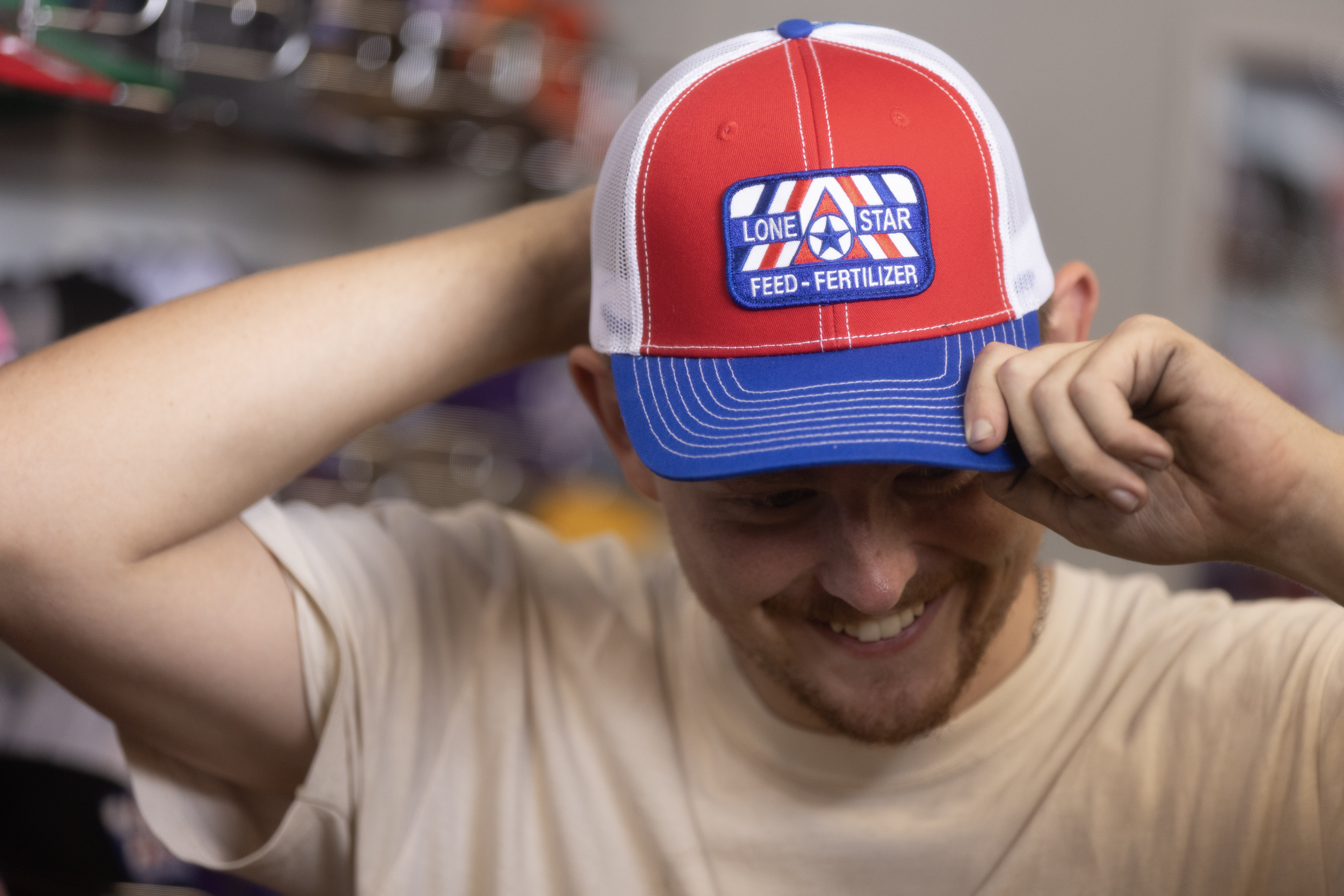 A smiling man putting on a Lone Star Feed baseball cap.