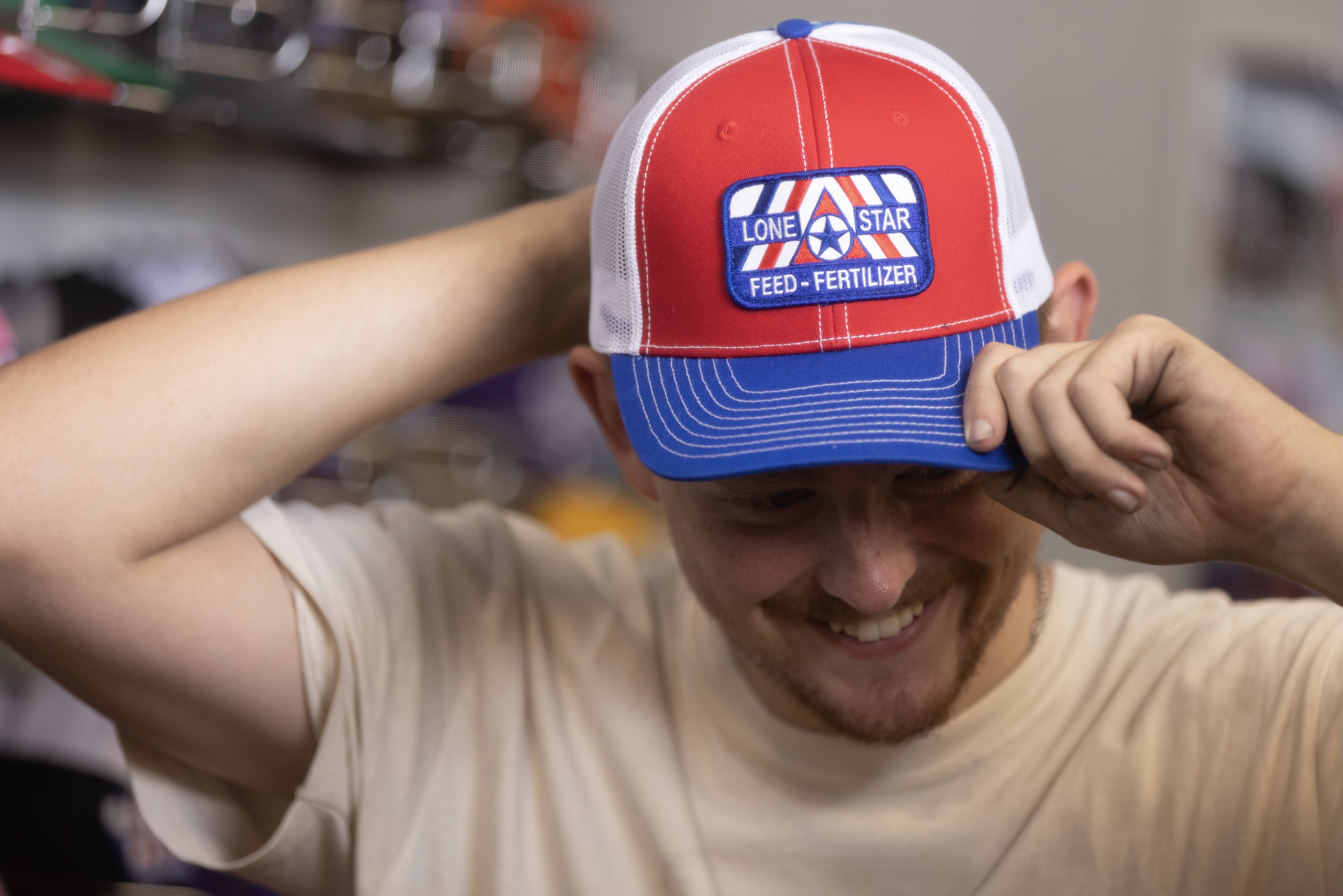A smiling man putting on a Lone Star Feed baseball cap.